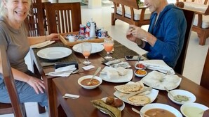 Une table à manger avec différents plats, notamment du riz, de la soupe et des galettes, dans une pièce dont le mobilier est en bois et où l’on aperçoit une plante au fond.