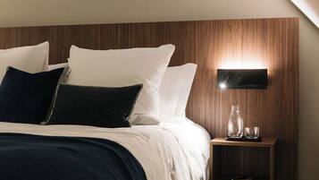 A modern bedroom with a sloped ceiling, a wooden headboard, a bedside table with a lamp, and a nightstand.