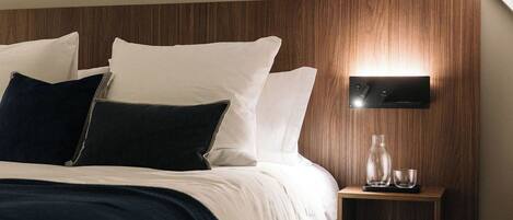 Un dormitorio moderno con techo inclinado, cabecera de madera, mesita de noche con lámpara y otro mueble auxiliar.