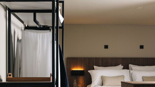 Une chambre d’hôtel avec des lits superposés, une table de chevet avec une lampe, une valise et une tête de lit en bois.