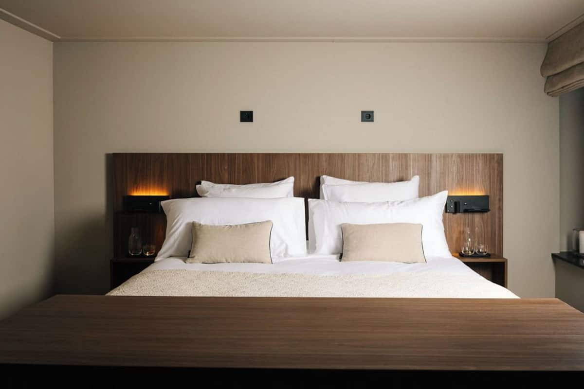 A neatly made bed with a wooden headboard, two bedside tables with lamps, and a small shelf with decorative items.
