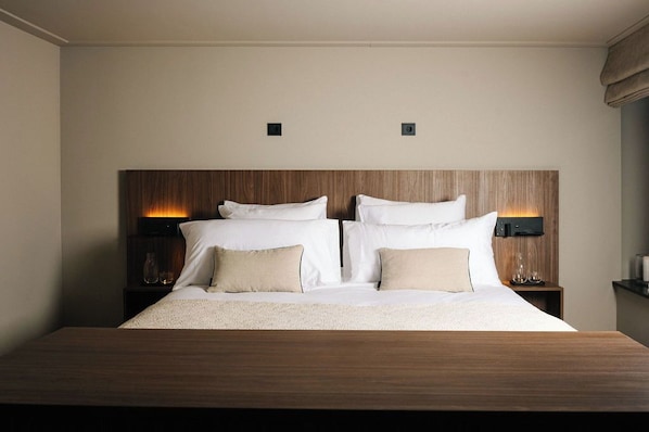 A neatly made bed with a wooden headboard, two bedside tables with lamps, and a small shelf with decorative items.