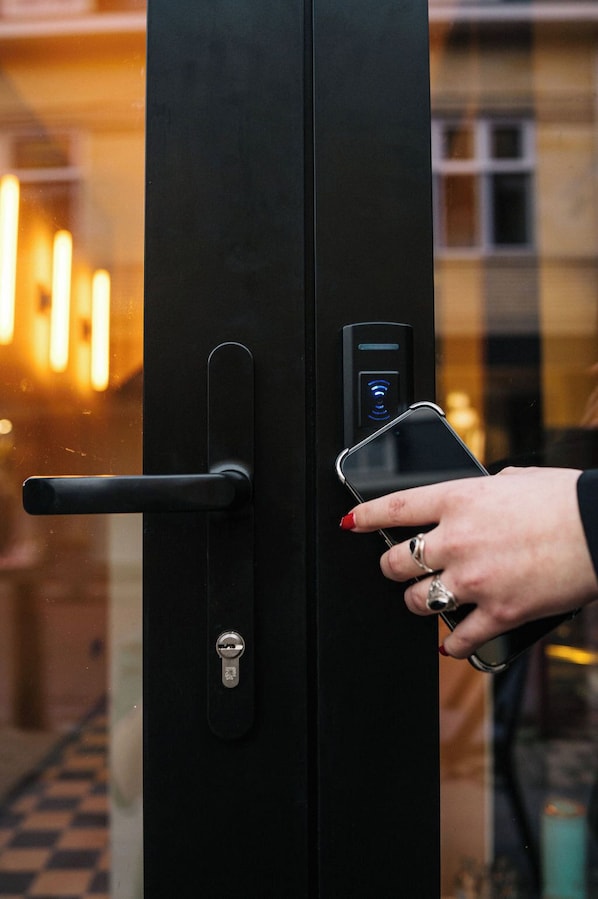 A person using a smartphone to unlock a door with a keyhole and a digital keypad. - Hotel BLINK (Valkenburg aan de Geul)