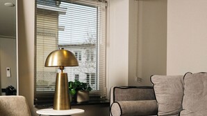Un salon moderne avec un fauteuil rond, un canapé avec des coussins, une petite table ronde avec une lampe et une fenêtre avec des stores.