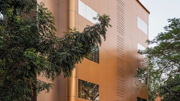 Un edificio moderno con fachada curva, amplios ventanales y un área ajardinada con plantas.