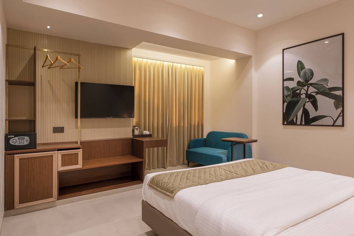 Ein modernes Hotelzimmer mit einem großen Bett, einem flachbildfernseher an der Wand, einer Sitzecke mit blauem Sessel und einer Holzkonsole mit Radio.