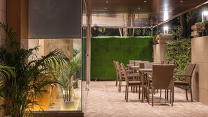 Un patio al aire libre con mobiliario de mimbre, plantas en macetas y una pared verde.