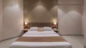 Una habitación de hotel moderna con una cama grande, dos mesitas de noche con lámparas, un cabecero con líneas verticales e iluminación empotrada en el techo.
