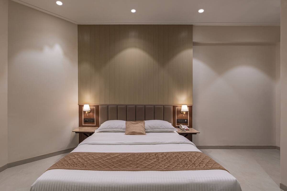 Ein modernes Hotelzimmer mit einem großen Bett, zwei Nachttischen mit Lampen, einer Kopfteil mit vertikalen Linien und Einbauleuchten.