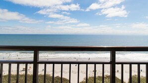 Uitzicht op een strand vanaf een balkon met een hekwerk, zandstrand en de oceaan.