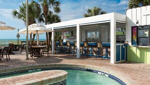 Un bar situé au bord de la piscine, avec des places assises en plein air et une vue sur l’océan.
