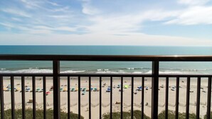 Une vue sur la plage depuis un balcon doté d’une balustrade, avec une plage de sable et l’océan en toile de fond.