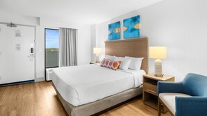 Habitación de hotel con una cama grande, dos lámparas de noche, un sillón azul y dos cuadros abstractos en la pared.