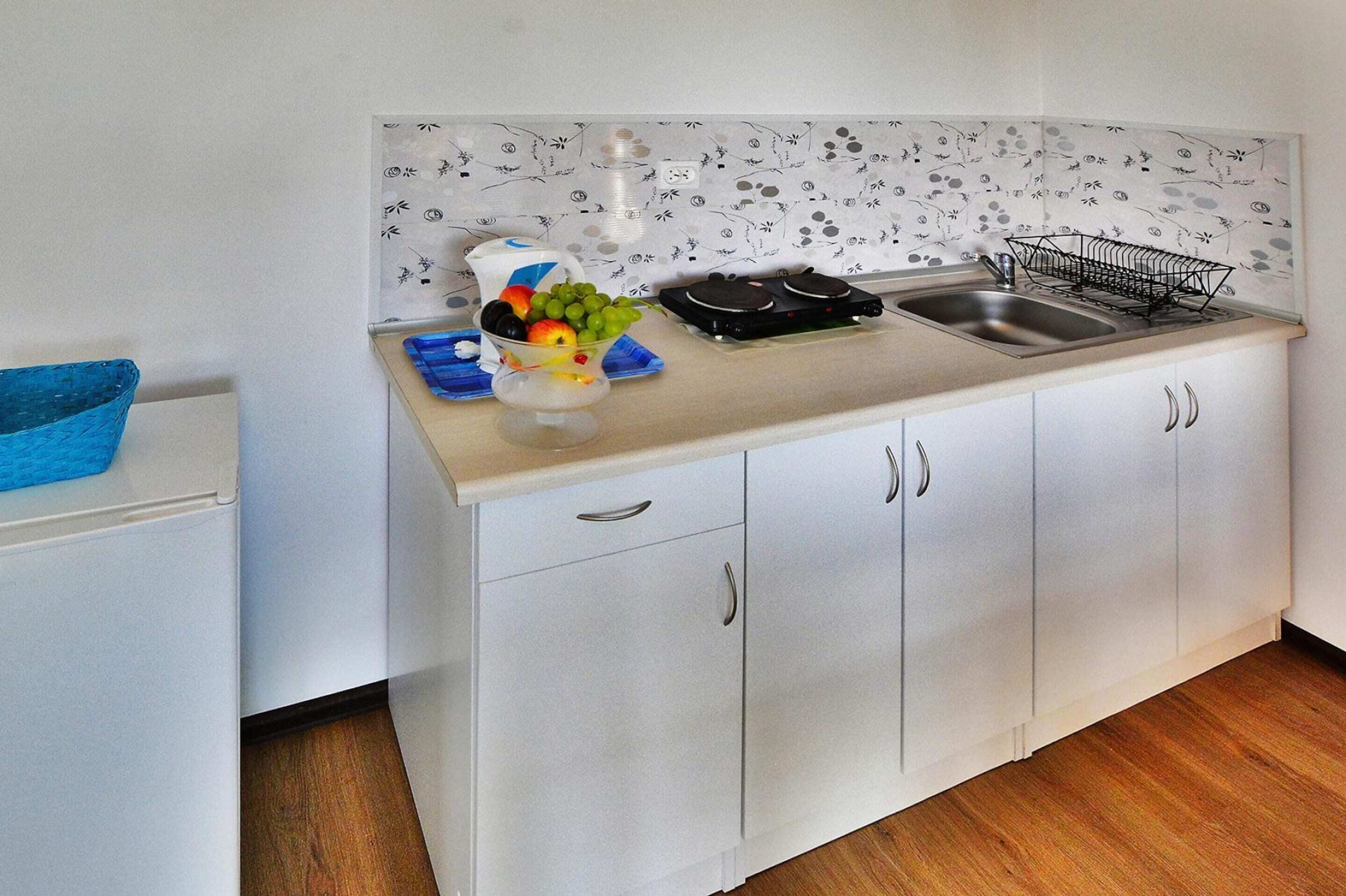 A small kitchen with white cabinets, a sink, and a fruit bowl on the counter.