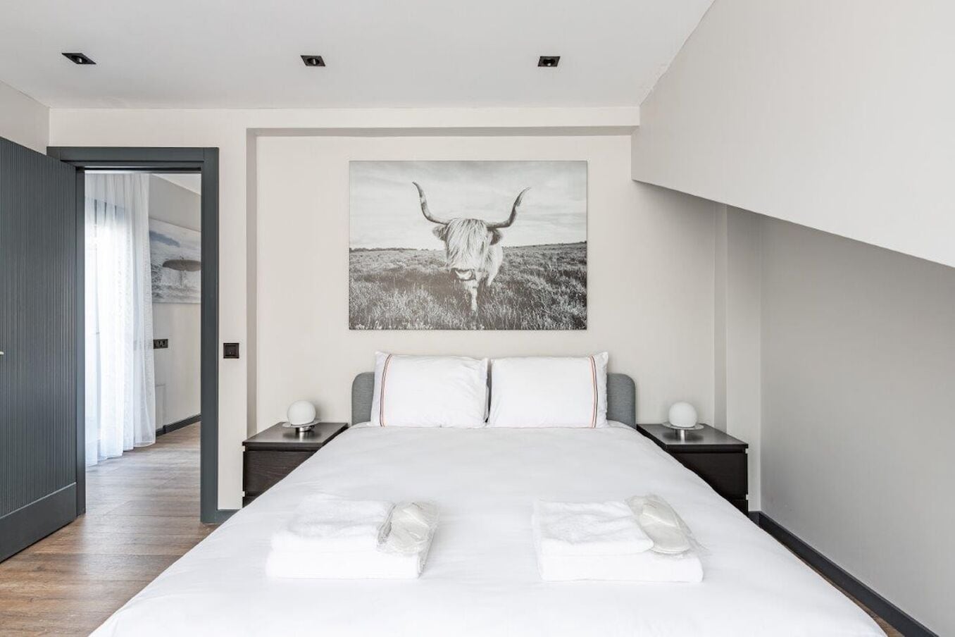 Un dormitorio moderno con una cama grande, dos mesitas de noche y una obra de arte colgada en la pared de un toro.