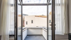 A balcony with a view of buildings, a door with a keyhole, and sheer curtains.