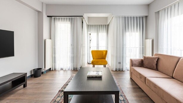 A modern living room with a sofa, a coffee table, a yellow armchair, and a television.