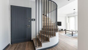 A modern interior with a curved staircase, a dark grey door, and a minimalist living area with a flat-screen TV.