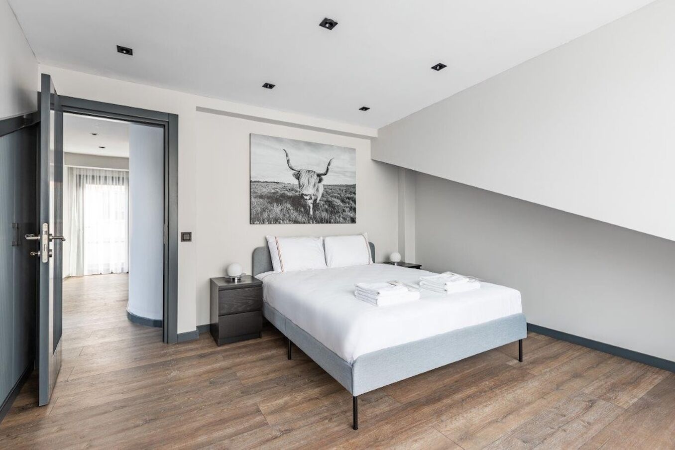 A modern bedroom with a bed, bedside tables, a nightstand, and a large window.