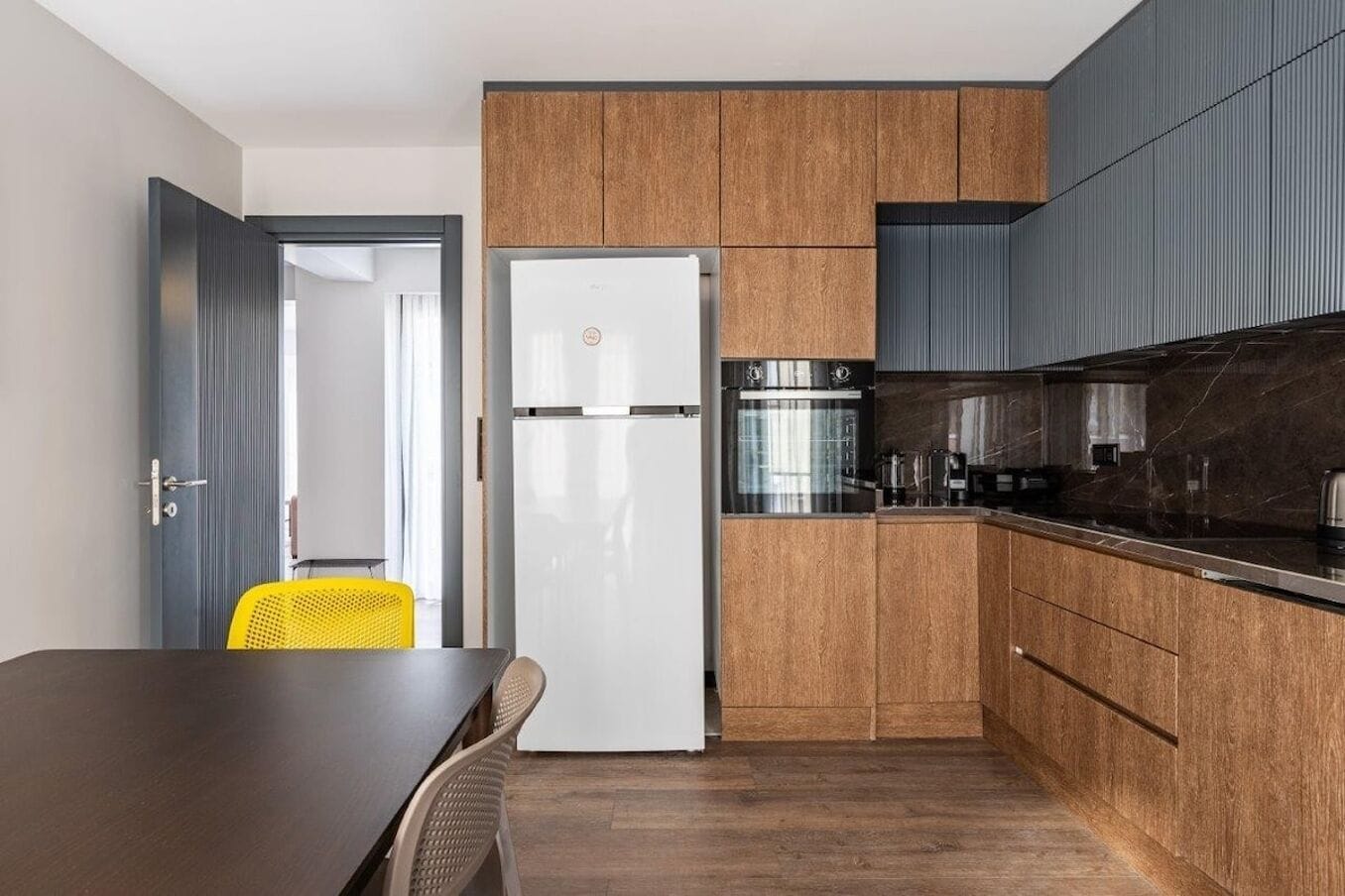 A modern kitchen with wooden cabinets, a white refrigerator, a black oven, and a dark countertop.