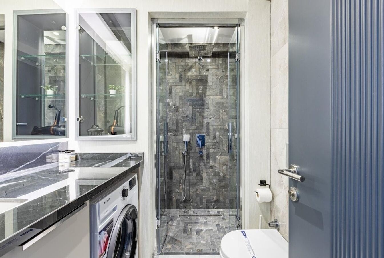 Een moderne badkamer met een douchecabine van glas, een marmeren aanrecht, een wasmachine en een toilet.