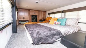 Quarto com cama, almofadas, mesa de cabeceira e janela com persianas.