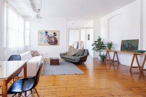 A spacious living room with a wooden floor, a grey sofa, a dining table with chairs, and a painting on the wall. - This apartment is a 1 bedroom(s), 1 bathrooms, located in Beyoğlu, İstanbul. (Beyoğlu)