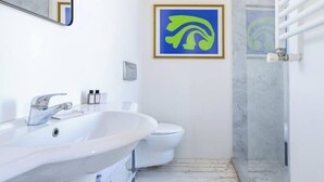 A bathroom with a white sink, a toilet, and a shower. There is a framed picture on the wall.