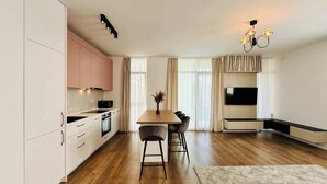 A modern kitchen with white cabinets, a wooden dining table, and a TV mounted on the wall. - Joy City Stay Nord One N2-1 (Timișoara)