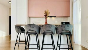 A modern kitchen with pink cabinets, a central island, and three bar stools. - Joy City Stay Nord One N2-1 (Timișoara)