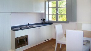 Une cuisine moderne avec des meubles blancs, un four encastré, un évier à deux bacs et une fenêtre donnant sur un paysage verdoyant.