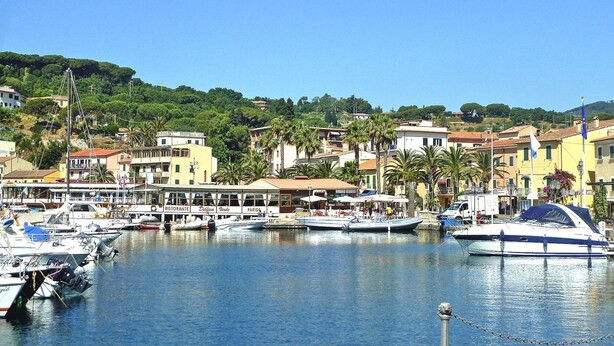 Un port de plaisance où sont amarrés des bateaux, un restaurant appelé « Ristorante Della Corte », et des bâtiments dotés de balcons donnant sur l’eau.