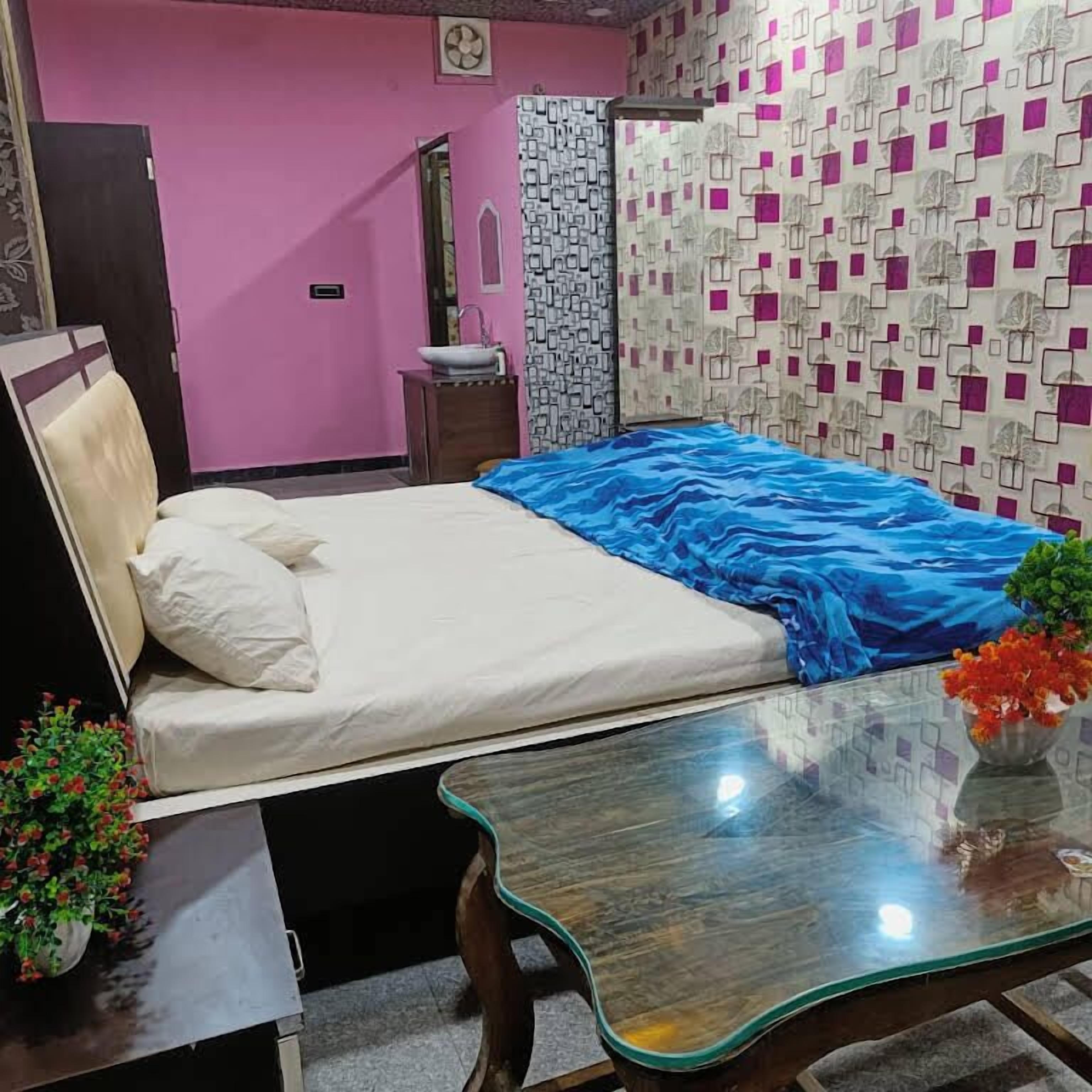 A bedroom with a bed, bedside table, and a small table with a vase of flowers.