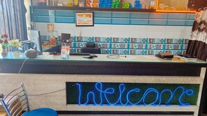 A reception desk with a neon 'Welcome' sign, a computer, and various items on the counter. - Tridev Restaurant By GRB (Muzaffarpur)