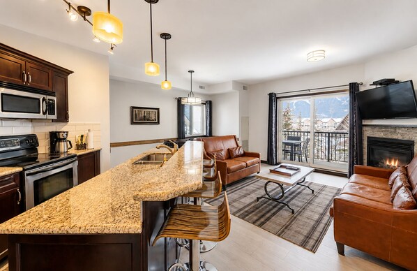 A modern kitchen with a large island, bar stools, and a dining area with a sofa and coffee table.