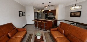 A modern living room with leather sofas, a coffee table, and a kitchen in the background.