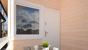 Una cabaña de madera con un ventanal grande, una puerta y una mesa de picnic con tazas blancas y una planta en maceta.