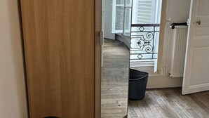A room with a wooden wardrobe, a large mirror reflecting a balcony with white shutters, and a black laundry basket on the floor. - Apartment near Montparnasse and Port Royal (Paris)
