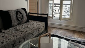 A living room with a glass coffee table, patterned sofa, and a view of a balcony through a window. - Apartment near Montparnasse and Port Royal (Paris)