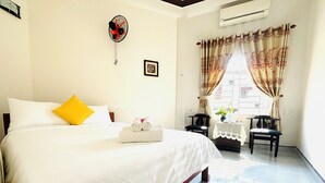A hotel room with a bed, a small table with a vase, two chairs, and a window with curtains. - Good Morning Hoi An Homestay and Hostel (Da Nang)