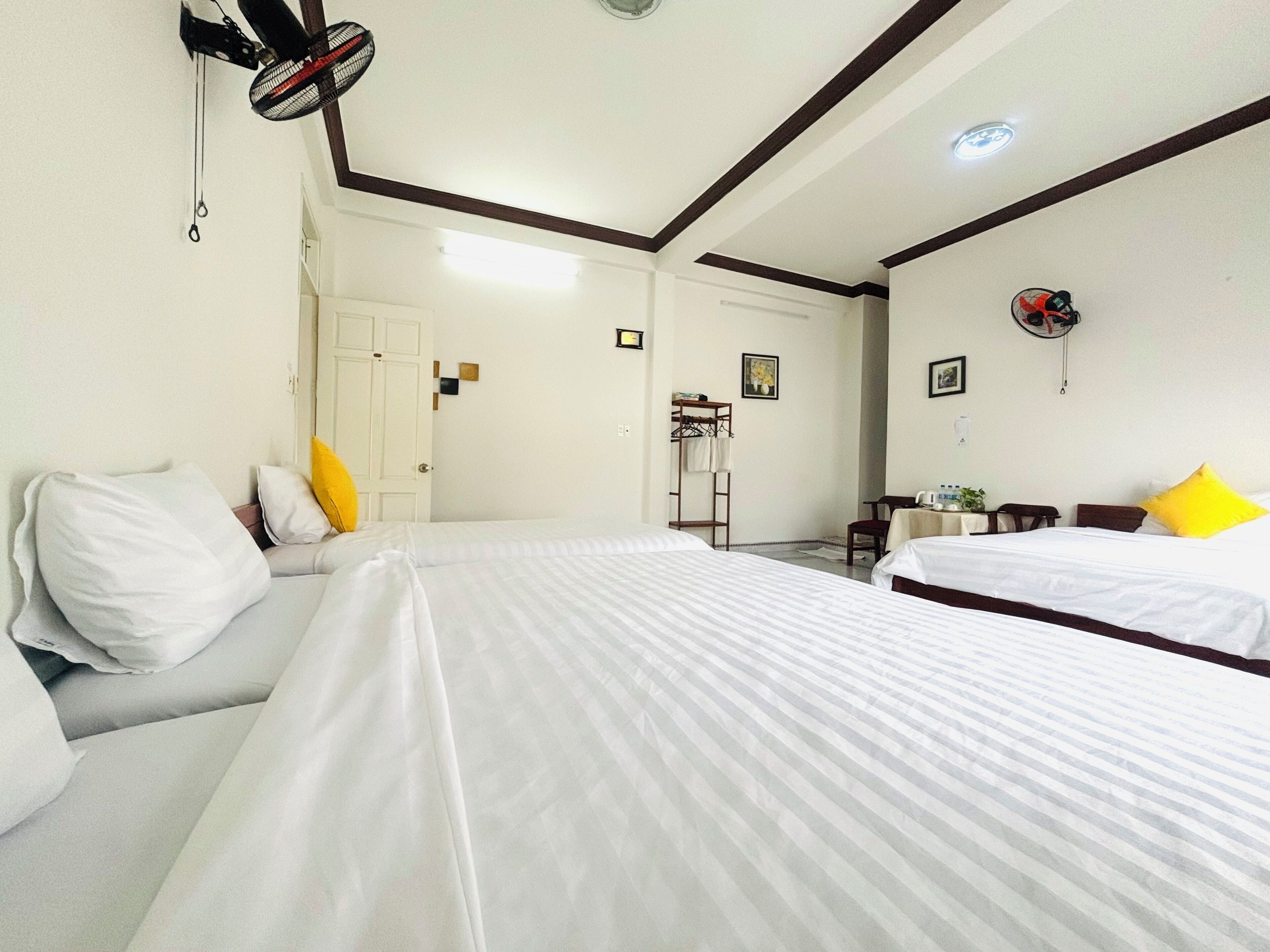 A hotel room with two beds, a small table, a chair, a coat rack, and a ceiling fan.