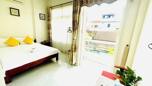 A hotel room with a large bed, a small table with a plant, and a view of the outside through a window. - Good Morning Hoi An Homestay and Hostel (Da Nang)