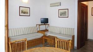 Ein Zimmer mit einer Couch, einem Fernseher, einem kleinen Tisch und einem runden Tisch mit Webmuster.