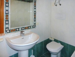 Un baño con lavamanos blanco, inodoro y espejo con detalles decorativos.