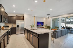 A modern kitchen with dark cabinetry, stainless steel appliances, a large island, and a flat-screen TV.