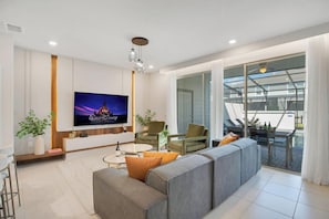A modern living room with a flat-screen TV, grey sofa, and a balcony with a glass door.