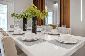 A modern dining area with a long table set for six, surrounded by chairs, and a decorative plant centerpiece.