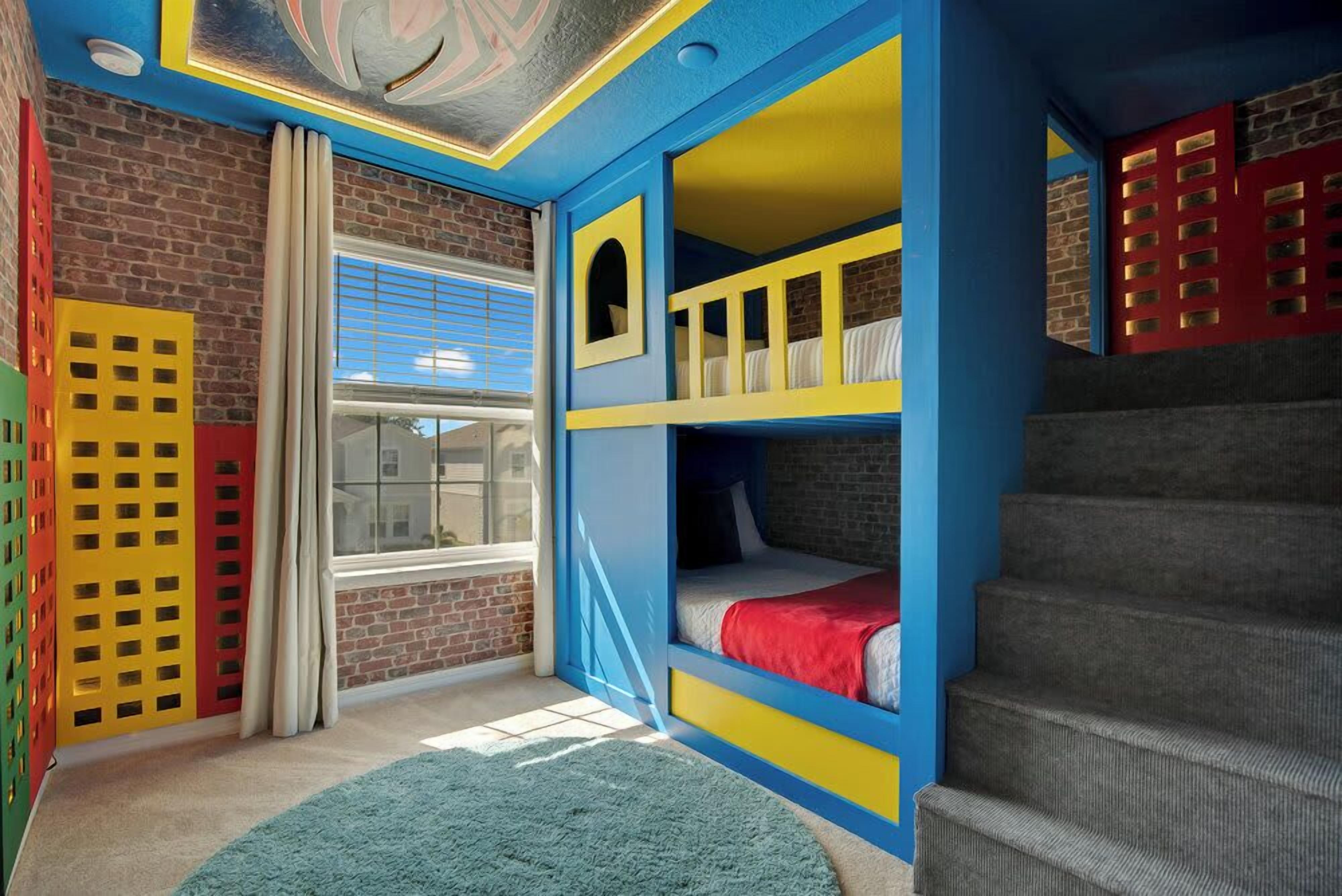 A room with bunk beds, a window with blinds, a brick wall, and a staircase.