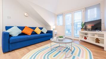 A modern living room with a blue sofa, colorful rug, and a TV on a white stand.