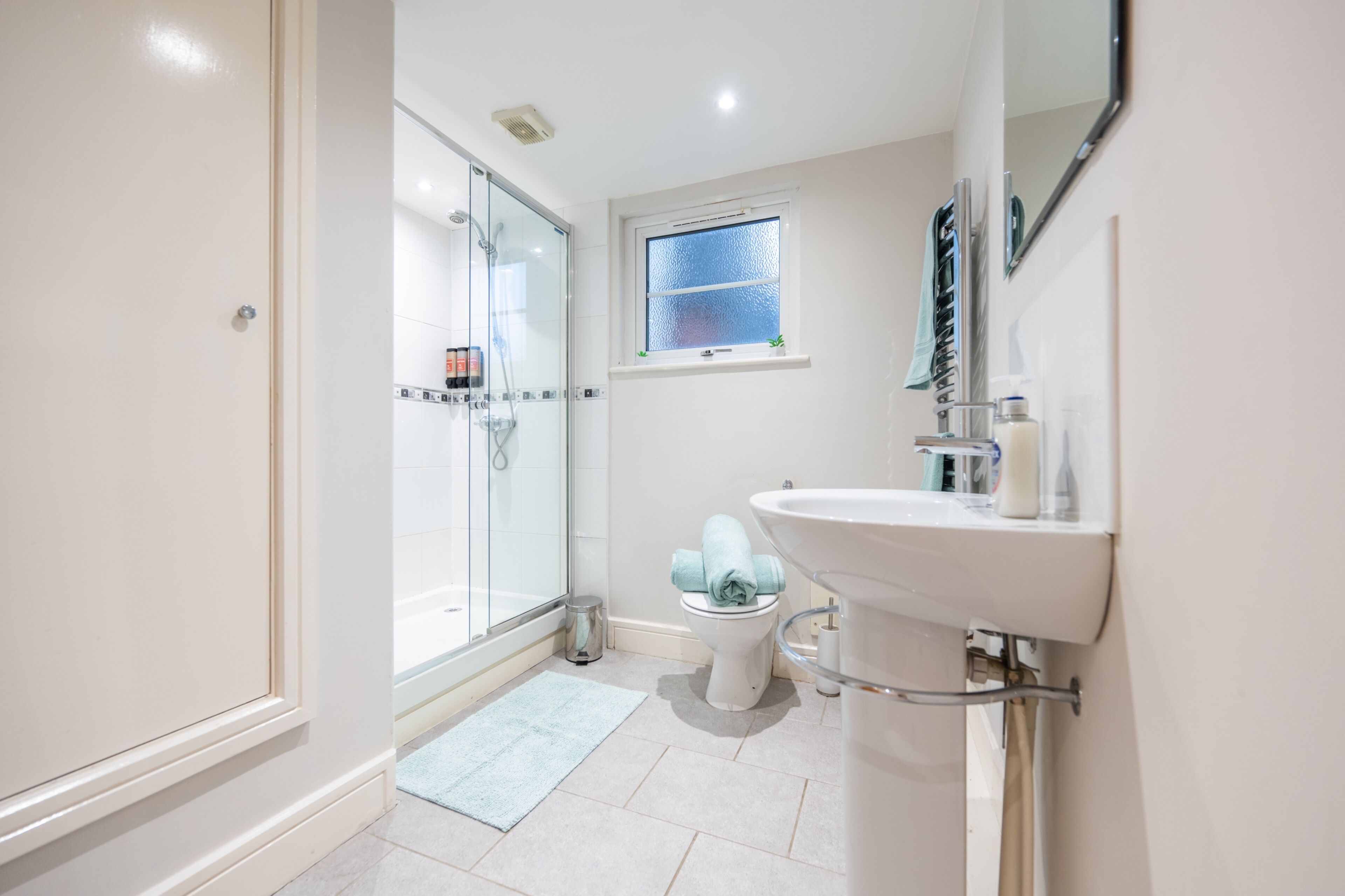 A modern bathroom with a glass-enclosed shower, a toilet, and a sink with a mirror above.